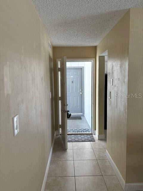 hall with a textured ceiling and light tile patterned floors