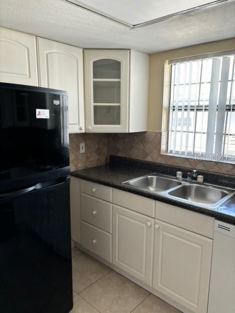 kitchen with light tile patterned floors, backsplash, white dishwasher, black fridge, and sink