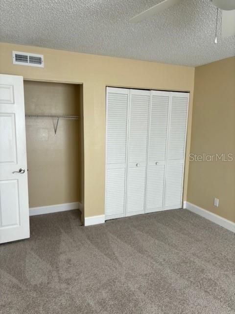 unfurnished bedroom with ceiling fan, carpet, and a textured ceiling