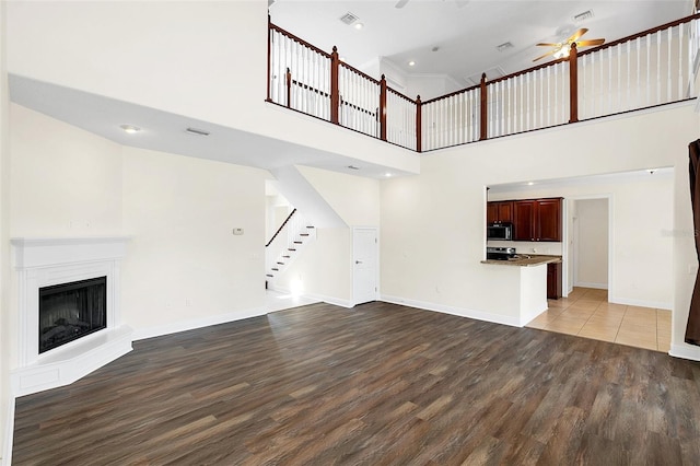 unfurnished living room with a towering ceiling, hardwood / wood-style flooring, and ceiling fan