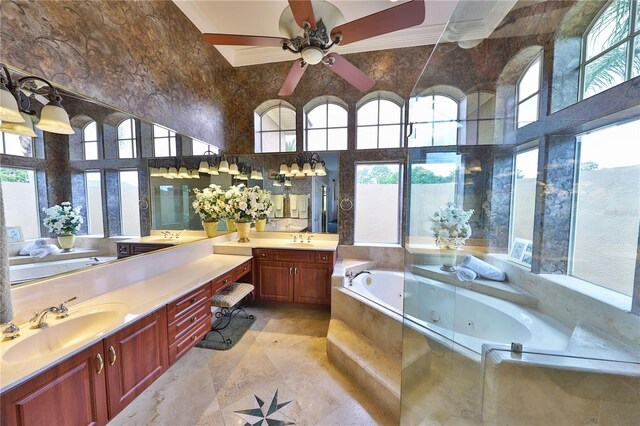 bathroom with ceiling fan, a high ceiling, tiled tub, vanity, and ornamental molding