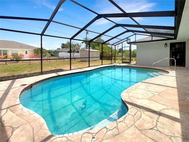 view of swimming pool with a lawn, glass enclosure, a storage unit, and a patio area