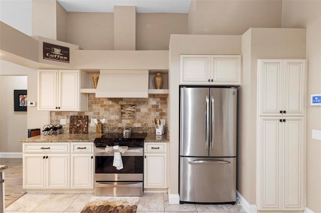 kitchen featuring premium range hood, dark stone countertops, backsplash, light tile patterned floors, and appliances with stainless steel finishes