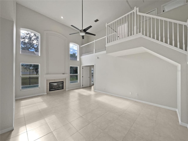 unfurnished living room with a tile fireplace, a high ceiling, light tile patterned floors, and ceiling fan