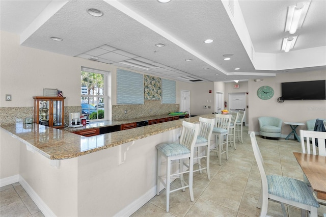 kitchen featuring light tile patterned flooring, a breakfast bar area, light stone counters, kitchen peninsula, and backsplash