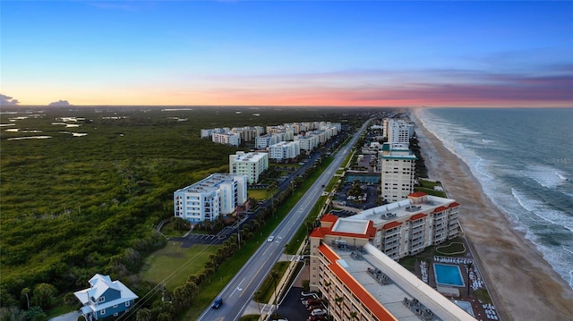 aerial view at dusk featuring a view of the beach and a water view