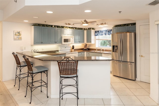 kitchen featuring sink, white appliances, a breakfast bar area, ceiling fan, and kitchen peninsula