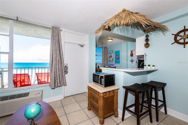 800 N Atlantic Ave Unit 301, Daytona Beach, FL 32118 - kitchen with stainless steel microwave, baseboards, light tile patterned flooring, a wall mounted air conditioner, and a breakfast bar