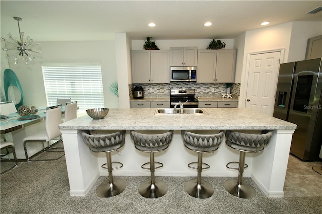 kitchen with gray cabinetry, sink, stainless steel appliances, and a kitchen island with sink