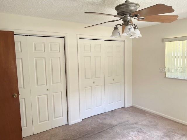 unfurnished bedroom with ceiling fan, two closets, carpet floors, and a textured ceiling