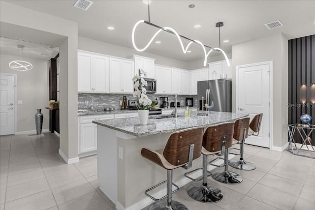 kitchen featuring appliances with stainless steel finishes, pendant lighting, backsplash, light tile patterned floors, and a kitchen island with sink