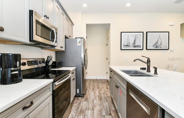 kitchen with light stone countertops, appliances with stainless steel finishes, light wood-type flooring, sink, and gray cabinets