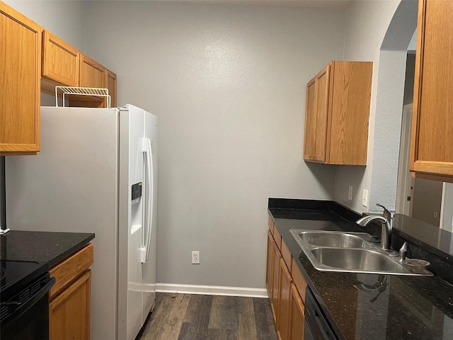 kitchen featuring sink, dark stone countertops, white fridge with ice dispenser, dishwashing machine, and dark hardwood / wood-style flooring