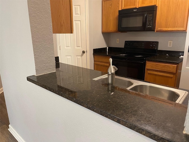 kitchen featuring dark stone countertops, dark wood-type flooring, black appliances, and sink