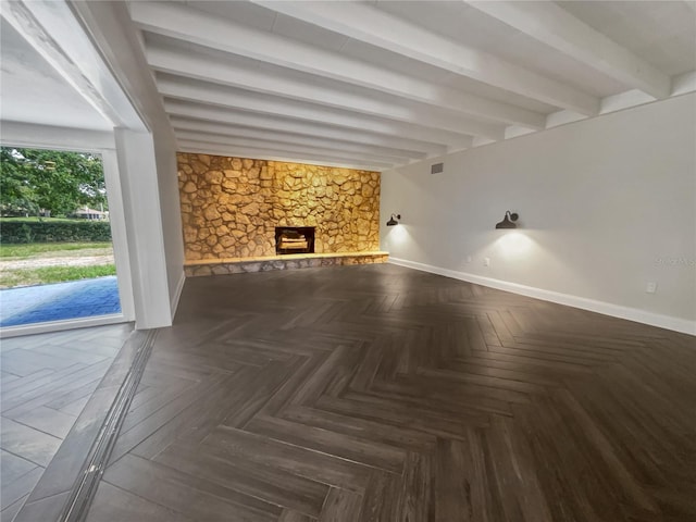 unfurnished living room featuring a stone fireplace, dark parquet floors, and beamed ceiling