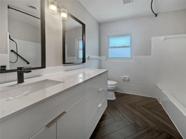 bathroom featuring vanity, toilet, parquet flooring, and tile walls