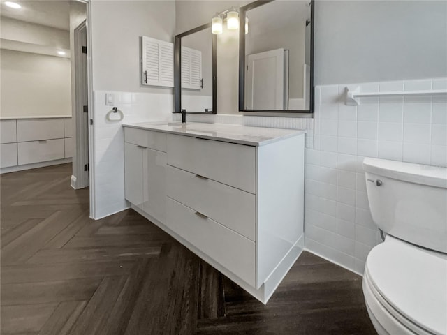 bathroom with parquet flooring, vanity, toilet, and tile walls