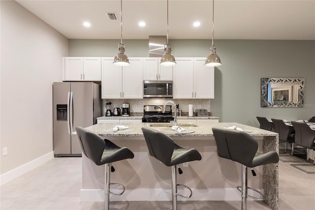 kitchen with appliances with stainless steel finishes, tasteful backsplash, white cabinetry, light stone counters, and a center island with sink