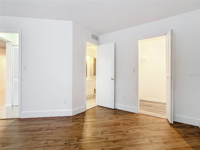 unfurnished bedroom featuring hardwood / wood-style floors, ensuite bathroom, a closet, and a walk in closet