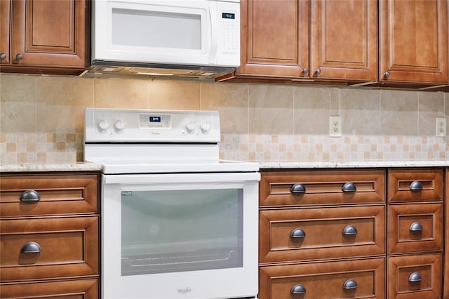 kitchen with backsplash, light stone counters, and white appliances