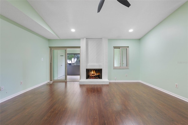 unfurnished living room with brick wall, ceiling fan, dark hardwood / wood-style floors, and a fireplace