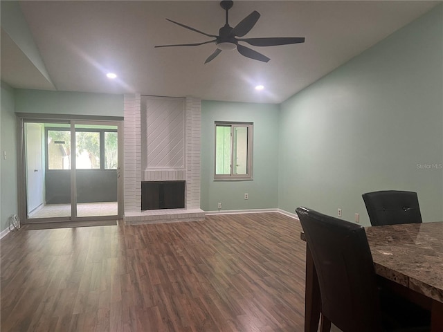 interior space featuring brick wall, vaulted ceiling, wood-type flooring, a brick fireplace, and ceiling fan