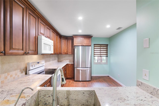 kitchen with white appliances, light hardwood / wood-style flooring, backsplash, and light stone counters