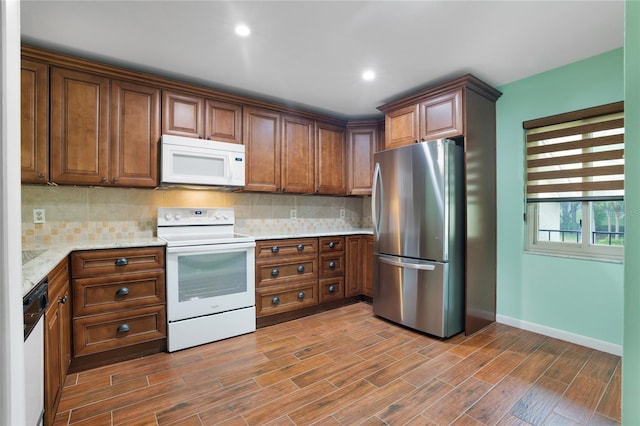 kitchen with hardwood / wood-style floors, light stone countertops, white appliances, and decorative backsplash