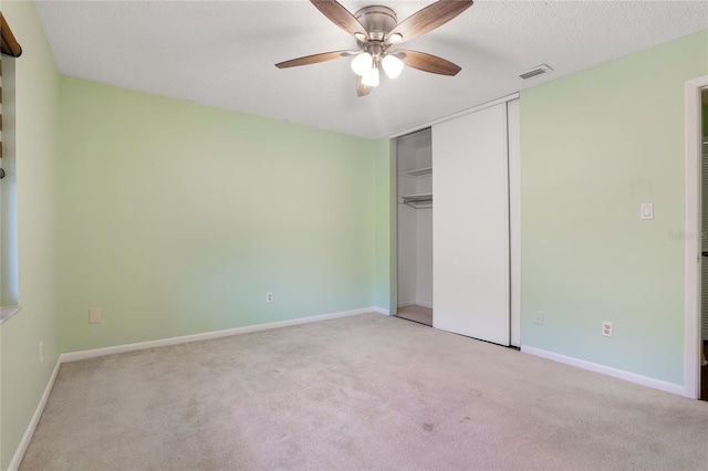 unfurnished bedroom with a textured ceiling, light colored carpet, ceiling fan, and a closet