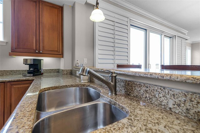 kitchen with hanging light fixtures, ornamental molding, light stone countertops, and sink