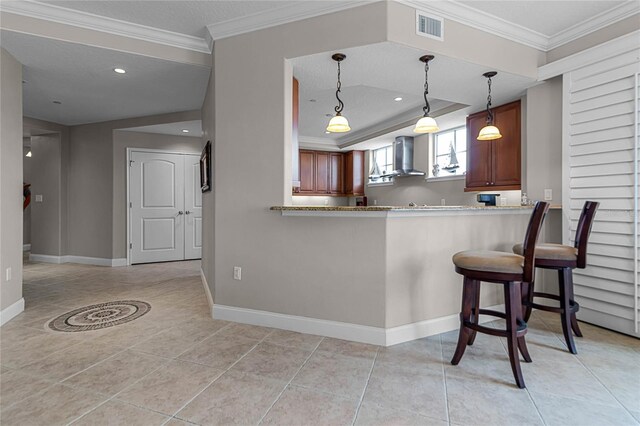 kitchen featuring decorative light fixtures, light tile patterned floors, kitchen peninsula, crown molding, and wall chimney exhaust hood