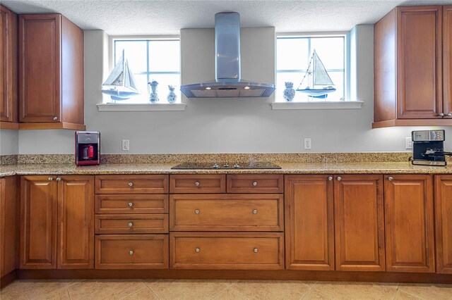 kitchen featuring black electric cooktop, light stone countertops, a textured ceiling, and wall chimney range hood