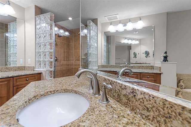 bathroom featuring tiled shower, vanity, and a textured ceiling