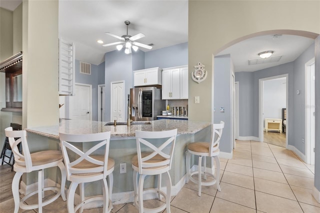 kitchen with white cabinets, stainless steel fridge, a kitchen bar, and light stone countertops