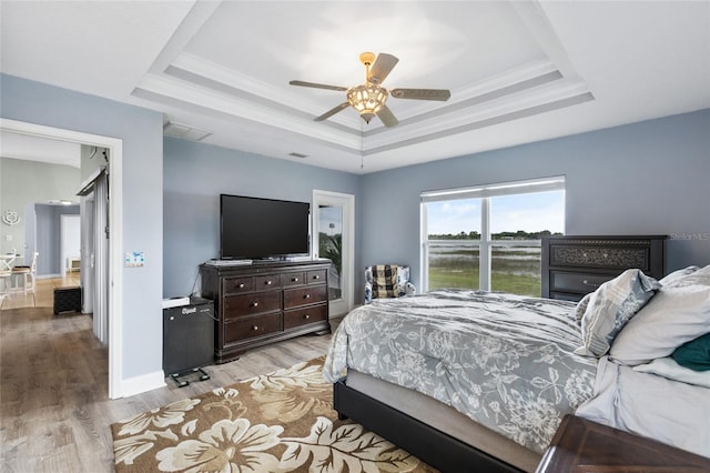 bedroom featuring ceiling fan, a raised ceiling, light wood-type flooring, and crown molding