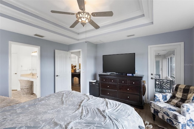 bedroom featuring dark hardwood / wood-style flooring, ensuite bathroom, a tray ceiling, ceiling fan, and crown molding