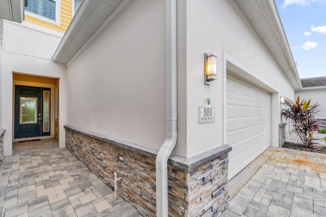 view of exterior entry with stone siding, an attached garage, and stucco siding