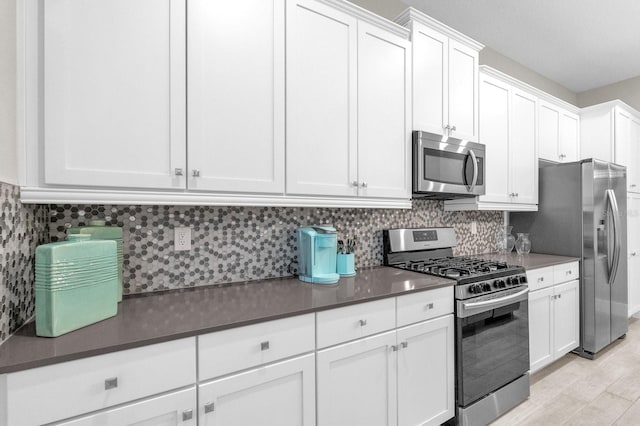 kitchen featuring white cabinets, appliances with stainless steel finishes, decorative backsplash, light wood finished floors, and dark countertops