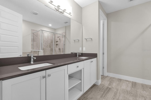 bathroom with double vanity, a stall shower, baseboards, and a sink