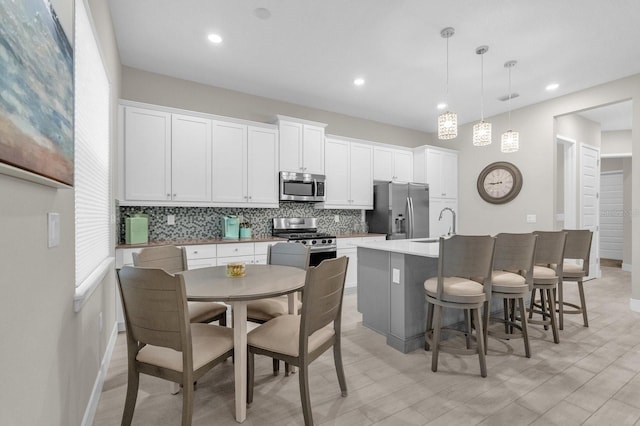 kitchen featuring a breakfast bar, decorative backsplash, appliances with stainless steel finishes, a kitchen island with sink, and white cabinetry