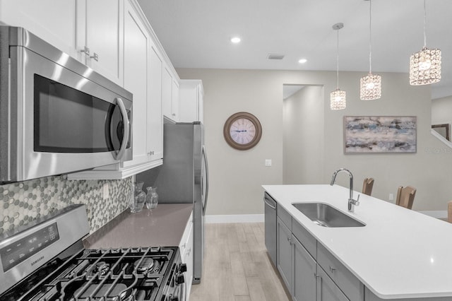 kitchen featuring a sink, appliances with stainless steel finishes, light wood-type flooring, tasteful backsplash, and a center island with sink