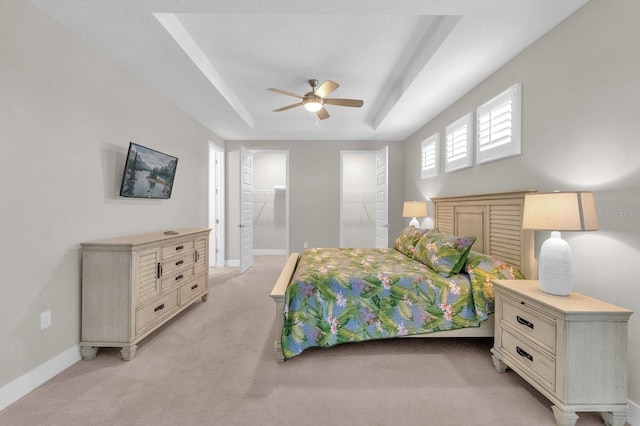 bedroom featuring light carpet, ceiling fan, a raised ceiling, and baseboards