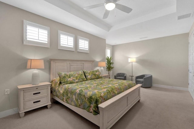 bedroom featuring light colored carpet, a ceiling fan, baseboards, visible vents, and a raised ceiling