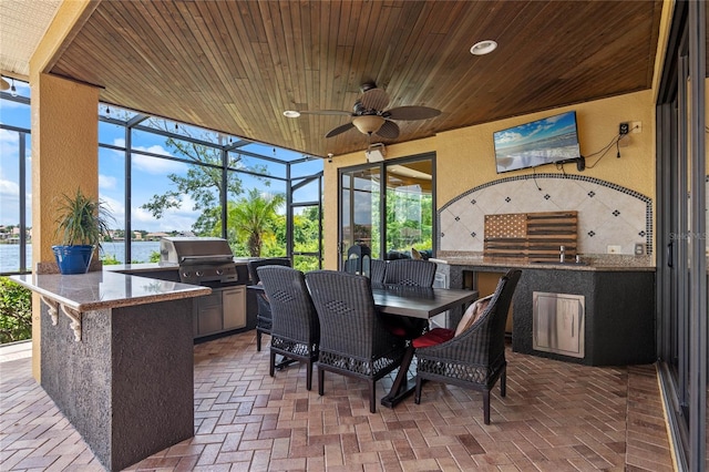 view of patio / terrace with an outdoor kitchen, ceiling fan, a water view, glass enclosure, and grilling area