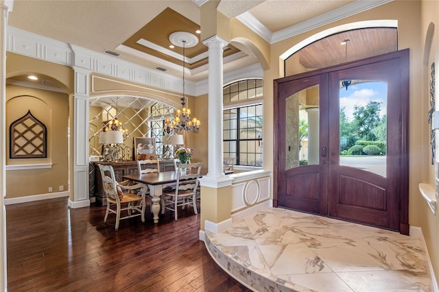 entryway with french doors, dark wood-type flooring, decorative columns, a chandelier, and ornamental molding