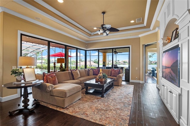 living room with dark hardwood / wood-style flooring, a raised ceiling, ceiling fan, and ornamental molding