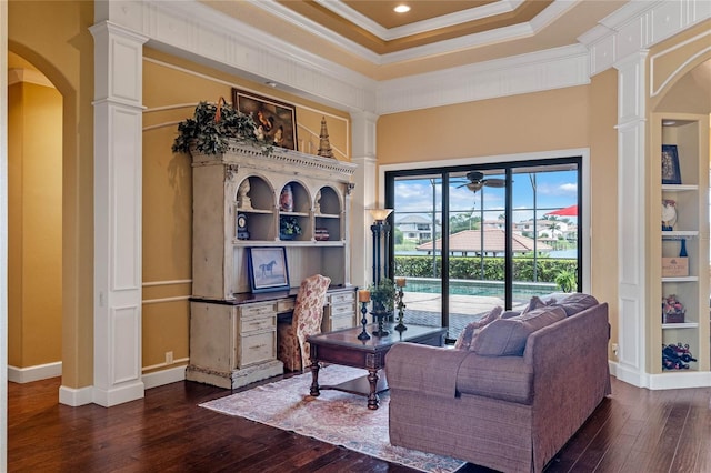 living room featuring decorative columns, a tray ceiling, dark wood-type flooring, and ornamental molding