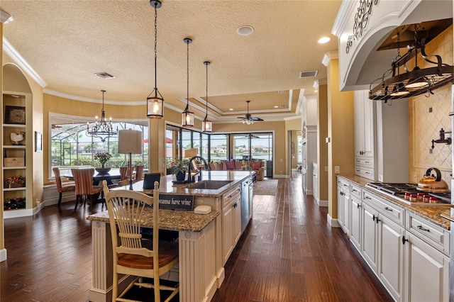 kitchen with a center island with sink, ceiling fan with notable chandelier, white cabinets, sink, and dark hardwood / wood-style flooring