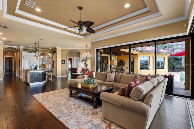 living room featuring ceiling fan with notable chandelier, dark hardwood / wood-style flooring, a raised ceiling, and crown molding