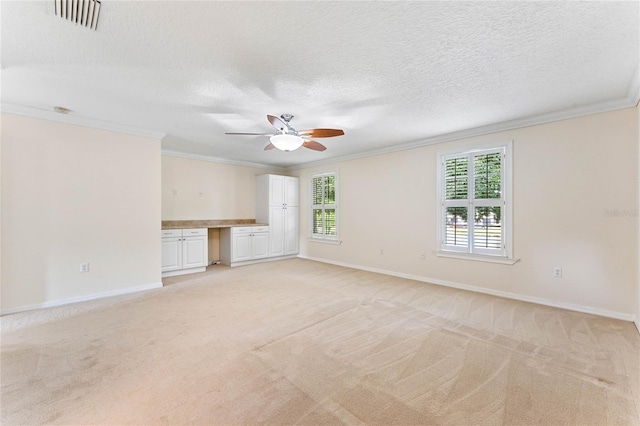 unfurnished living room featuring ceiling fan, crown molding, light colored carpet, a textured ceiling, and built in desk